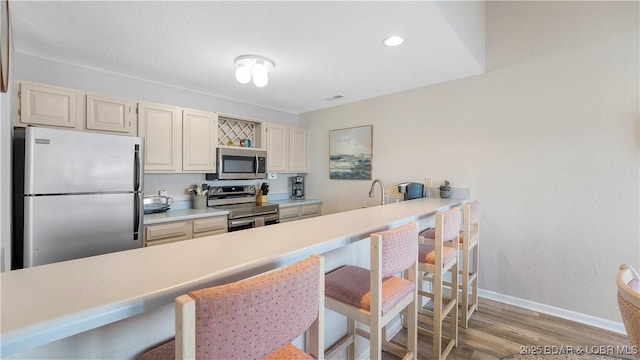 kitchen with stainless steel appliances, a breakfast bar, baseboards, light wood-style floors, and light countertops