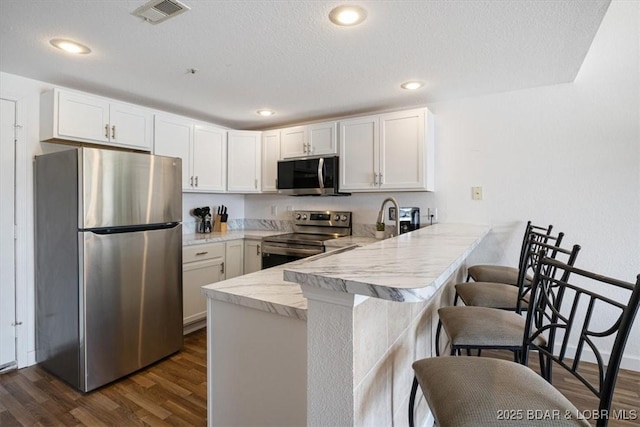 kitchen featuring stainless steel appliances, a peninsula, visible vents, a kitchen breakfast bar, and light countertops