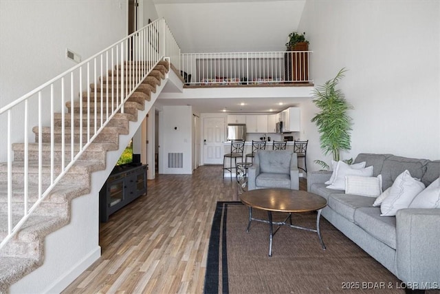 living room featuring baseboards, visible vents, a towering ceiling, stairs, and light wood-type flooring