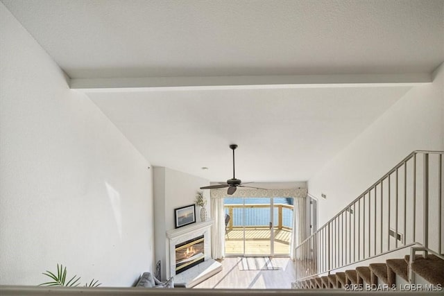 living area featuring lofted ceiling with beams, stairway, a ceiling fan, and a glass covered fireplace