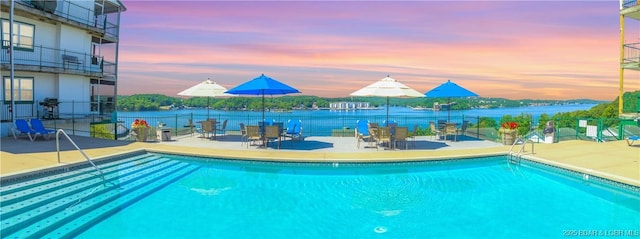 pool at dusk featuring a water view, a patio area, and a community pool