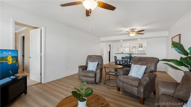 living area with a ceiling fan, crown molding, baseboards, and wood finished floors