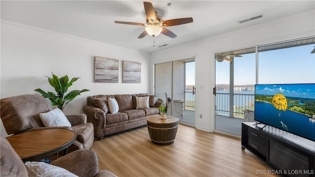 living room featuring light wood finished floors, ceiling fan, visible vents, and crown molding