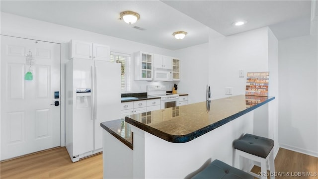 kitchen with a breakfast bar, glass insert cabinets, light wood-type flooring, white appliances, and a peninsula