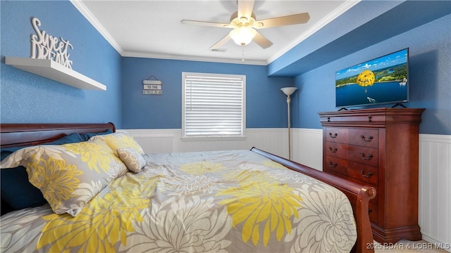 bedroom with a ceiling fan, wainscoting, visible vents, and crown molding