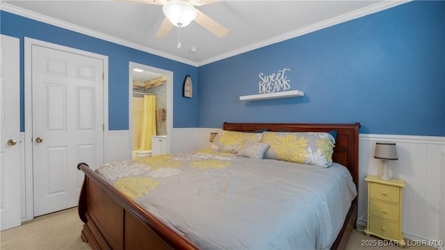 carpeted bedroom with ornamental molding, ensuite bathroom, a ceiling fan, and wainscoting