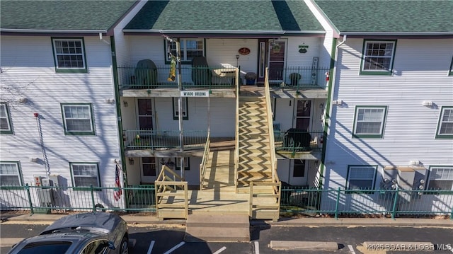 multi unit property featuring roof with shingles, fence, and a balcony