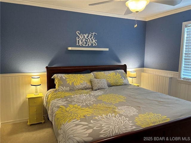 carpeted bedroom featuring a ceiling fan, a textured wall, wainscoting, and crown molding