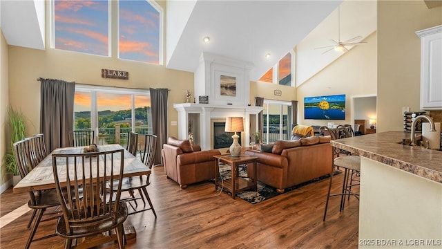 living area featuring ceiling fan, high vaulted ceiling, dark wood-type flooring, and a glass covered fireplace