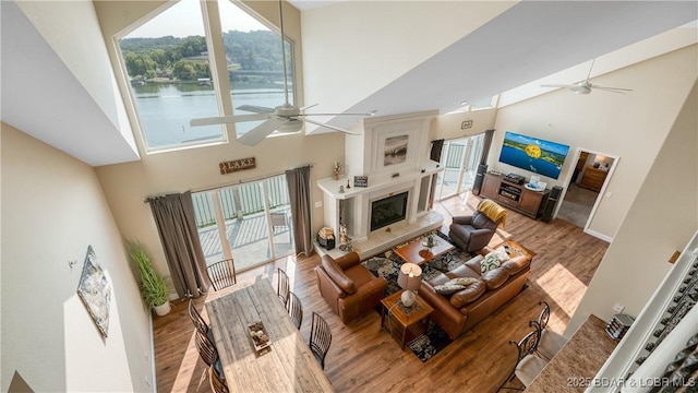 living area with high vaulted ceiling, wood finished floors, a ceiling fan, and a high end fireplace