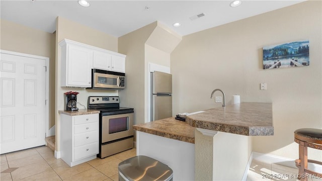 kitchen featuring visible vents, white cabinets, a kitchen breakfast bar, a peninsula, and stainless steel appliances