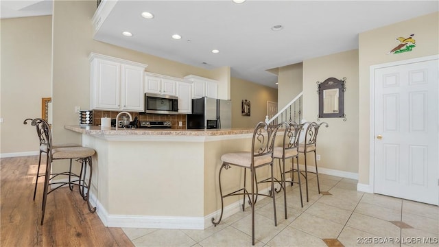 kitchen with a breakfast bar, backsplash, appliances with stainless steel finishes, white cabinets, and light tile patterned flooring