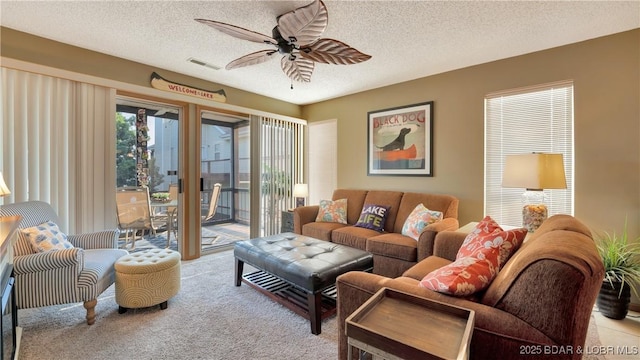 living area featuring light carpet, a ceiling fan, visible vents, and a textured ceiling