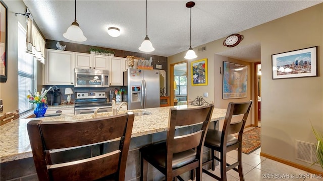 kitchen featuring a textured ceiling, appliances with stainless steel finishes, a sink, and pendant lighting