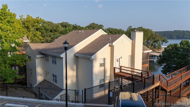 exterior space with a shingled roof, a water view, fence, and a chimney