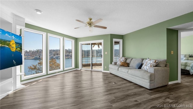 living room with a water view, ceiling fan, a textured ceiling, wood finished floors, and baseboards