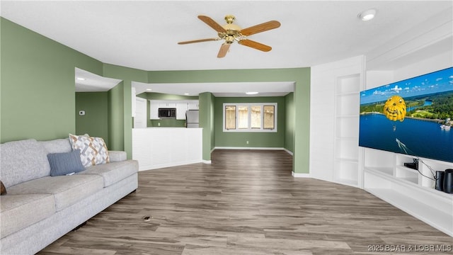 living room with built in shelves, wood finished floors, a ceiling fan, and baseboards