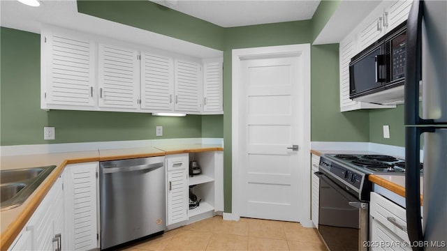 kitchen featuring light tile patterned floors, white cabinets, light countertops, black appliances, and a sink