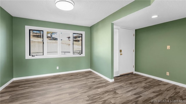 unfurnished room featuring a textured ceiling, baseboards, and wood finished floors