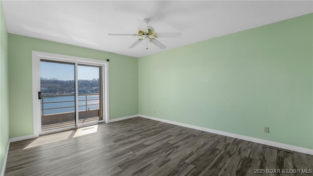 spare room featuring dark wood-type flooring, a water view, ceiling fan, and baseboards