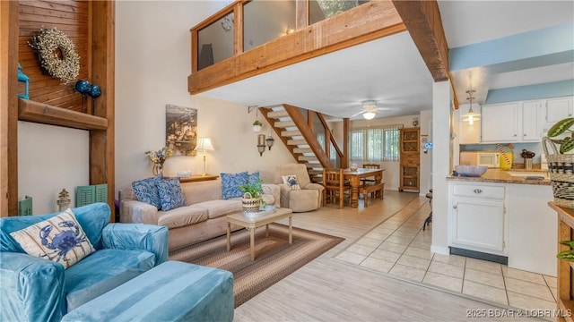 living room featuring light wood-type flooring, a ceiling fan, stairway, and beam ceiling