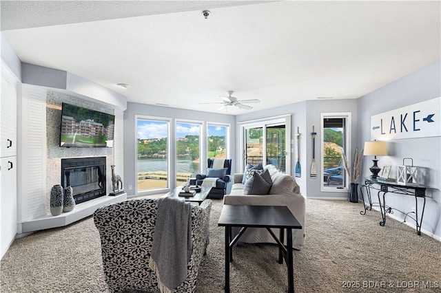 living area featuring baseboards, a ceiling fan, carpet flooring, and a glass covered fireplace