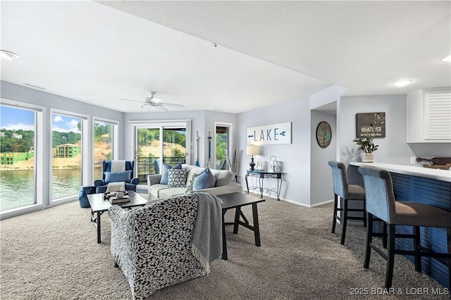 carpeted living area with ceiling fan, a bar, a water view, and baseboards