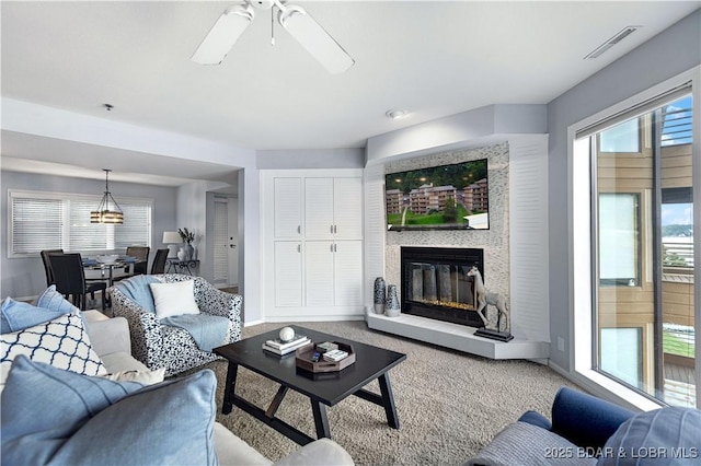 living room featuring ceiling fan, visible vents, baseboards, carpet, and a glass covered fireplace