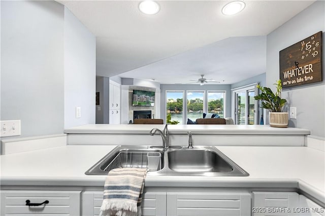 kitchen with light countertops, a ceiling fan, a large fireplace, open floor plan, and a sink