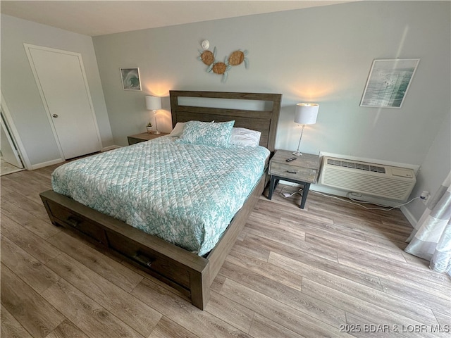 bedroom featuring an AC wall unit, baseboards, and wood finished floors