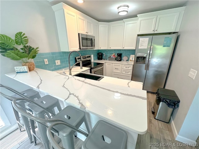 kitchen with stainless steel appliances, a peninsula, a sink, light wood-type flooring, and decorative backsplash