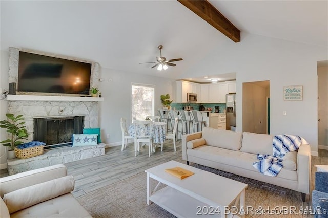 living area with vaulted ceiling with beams, ceiling fan, a fireplace, wood finished floors, and baseboards