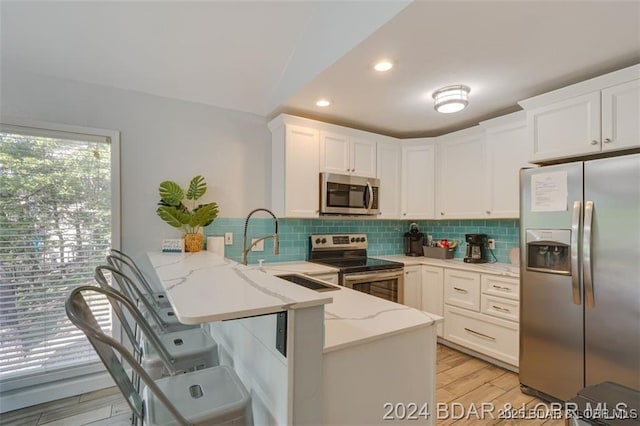 kitchen featuring light stone counters, stainless steel appliances, backsplash, light wood-style flooring, and a peninsula