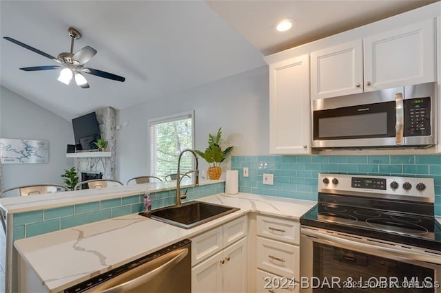 kitchen with appliances with stainless steel finishes, a peninsula, a sink, a fireplace, and backsplash