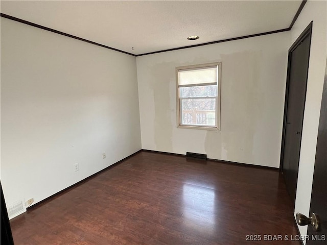 empty room with baseboards, wood finished floors, and crown molding