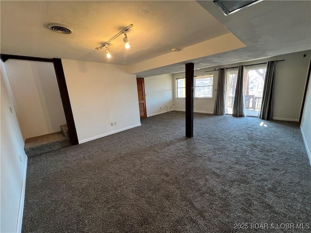 empty room featuring dark colored carpet, visible vents, stairway, track lighting, and baseboards