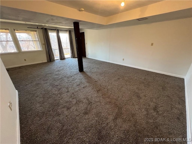 spare room featuring a tray ceiling, dark carpet, and baseboards