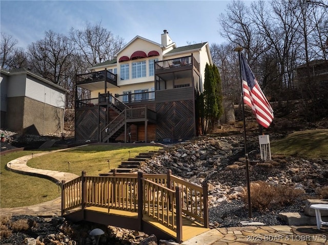 back of house with stairs, a lawn, a chimney, and a balcony