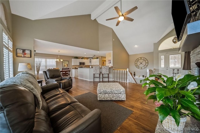 living area with high vaulted ceiling, ceiling fan with notable chandelier, baseboards, beam ceiling, and dark wood-style floors