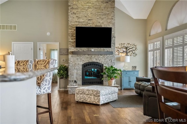 living room featuring high vaulted ceiling, a brick fireplace, dark wood-style flooring, and visible vents