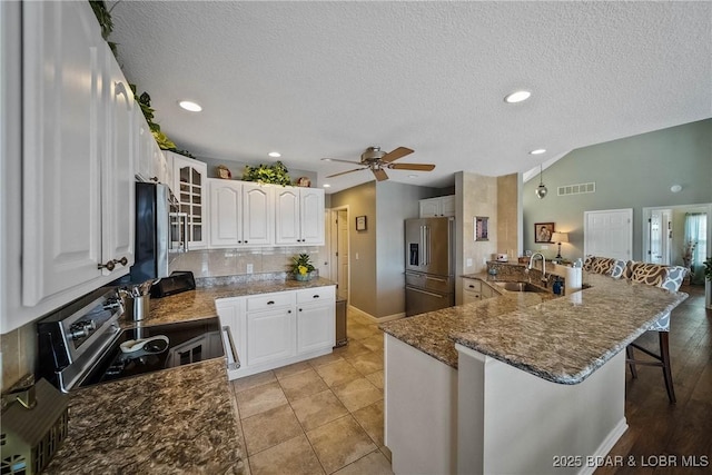 kitchen featuring appliances with stainless steel finishes, a breakfast bar, dark stone countertops, vaulted ceiling, and a sink