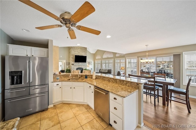 kitchen featuring white cabinets, a peninsula, light stone countertops, stainless steel appliances, and a fireplace