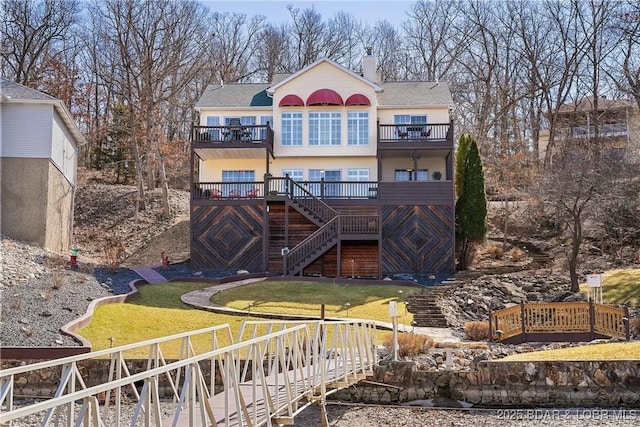 rear view of property featuring a yard, stairway, a chimney, and a balcony