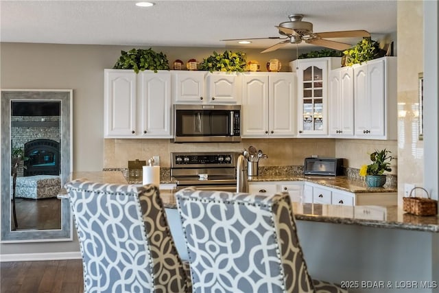 kitchen featuring stone counters, stainless steel appliances, white cabinets, decorative backsplash, and glass insert cabinets