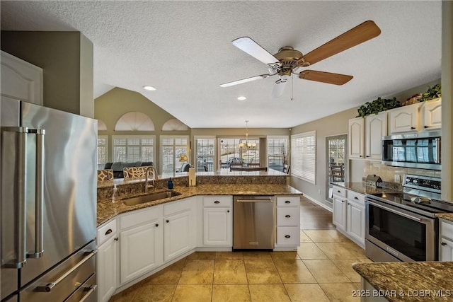 kitchen featuring light tile patterned floors, white cabinets, dark stone counters, stainless steel appliances, and a sink