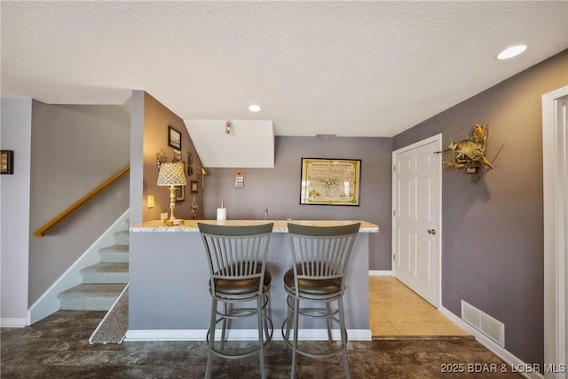 kitchen featuring a breakfast bar area, recessed lighting, a peninsula, visible vents, and baseboards