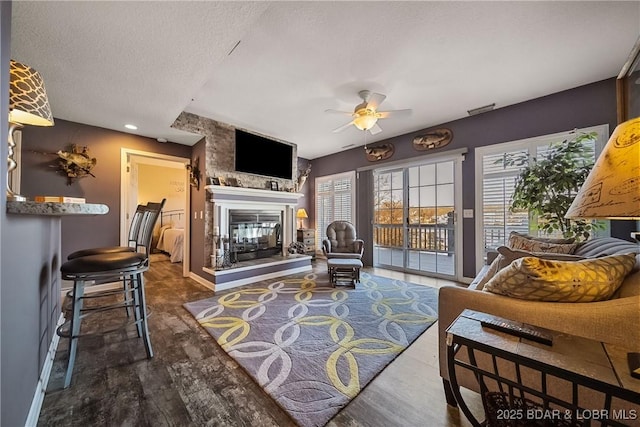 living area featuring a textured ceiling, wood finished floors, a multi sided fireplace, a ceiling fan, and baseboards