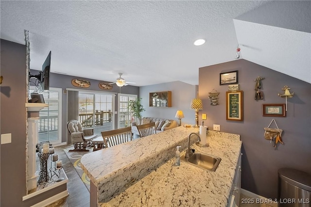 kitchen with baseboards, a ceiling fan, a textured ceiling, a fireplace, and a sink