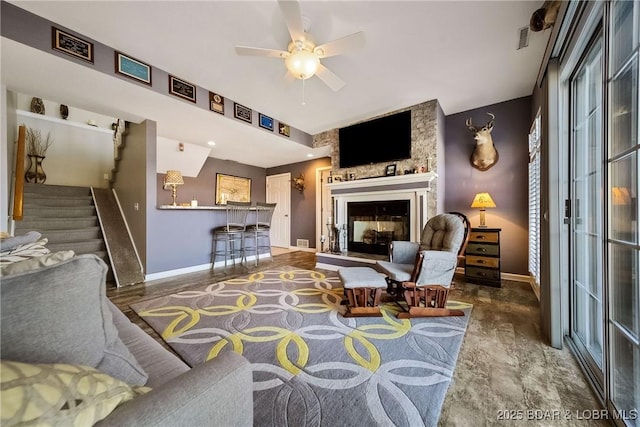 living area with stairs, ceiling fan, a fireplace, and baseboards