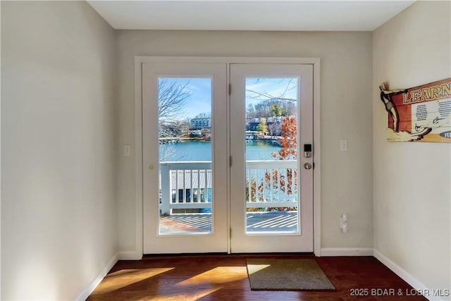 doorway to outside featuring a water view, plenty of natural light, baseboards, and dark wood-style flooring